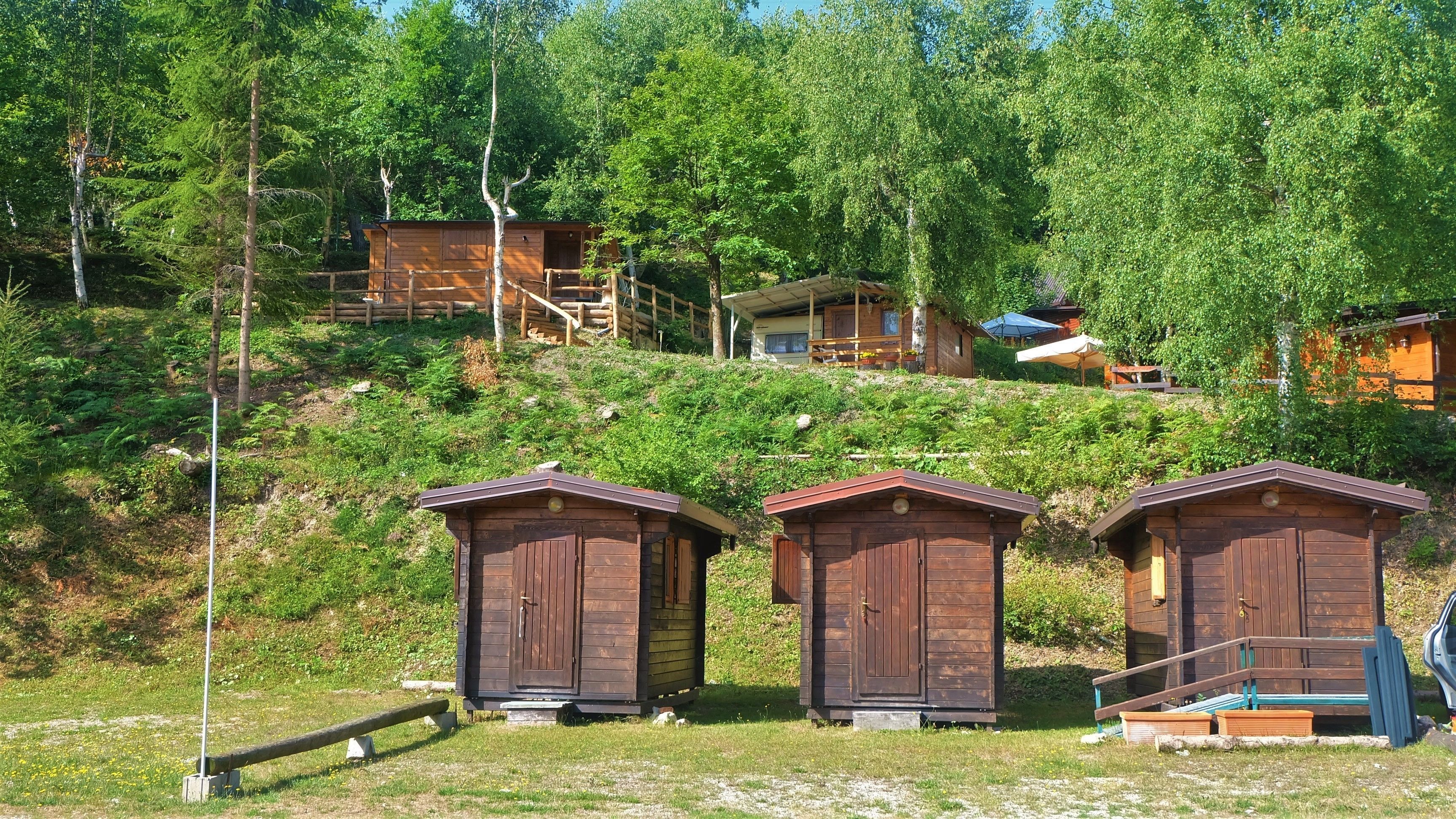 Tres cabañas de madera con un paisaje montañoso natural, una cerca de madera y un vehículo estacionado.