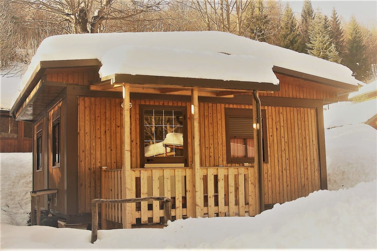 Una cabaña de madera con un porche y una ventana, rodeada de nieve.