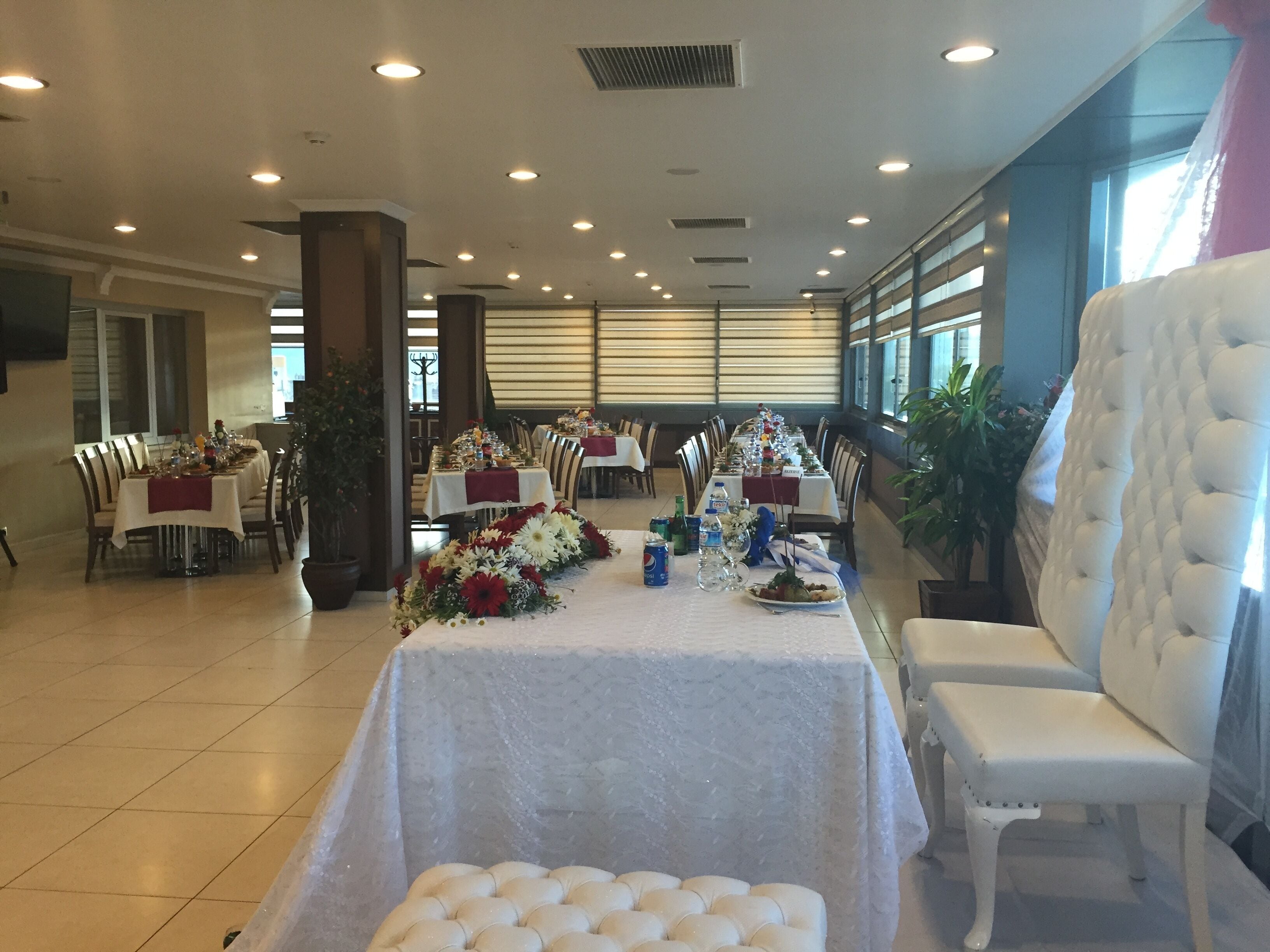 Une salle de banquet avec de nombreuses tables dressées pour le repas, des chaises et des plantes en pot.