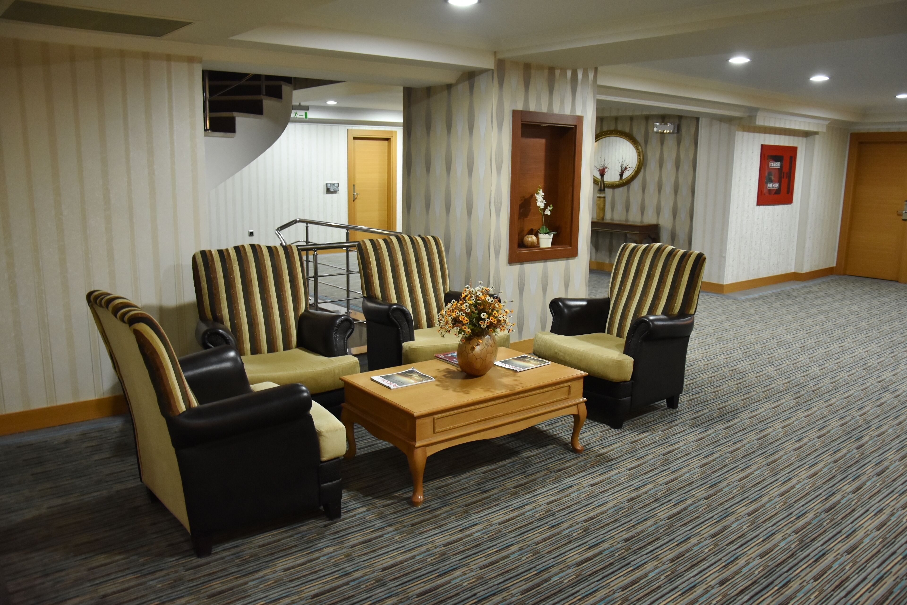 A hotel lobby with striped sofas, a wooden coffee table with a vase of flowers, and a patterned carpet.
