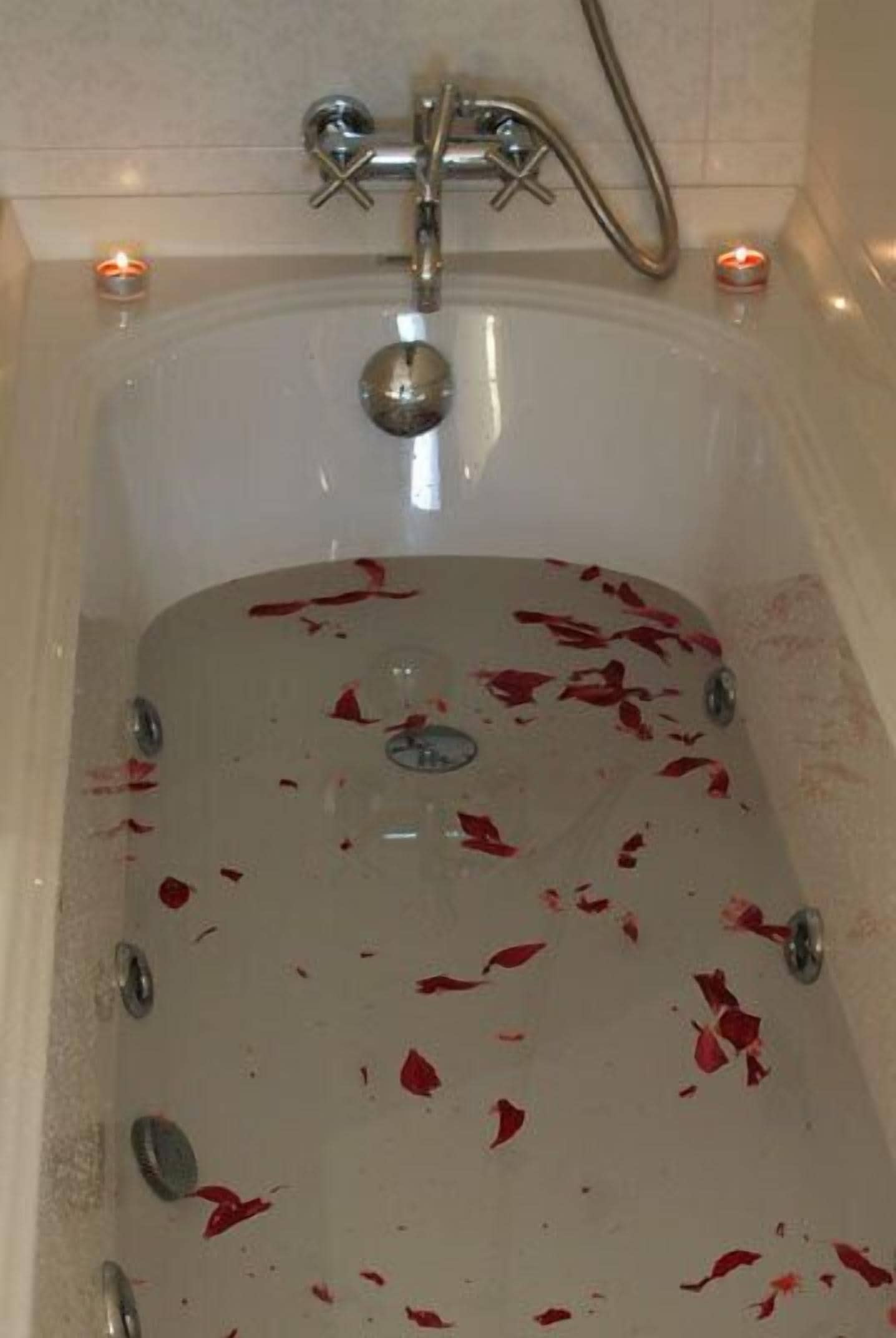 Una bañera con pétalos de rosa roja esparcidos en su interior.