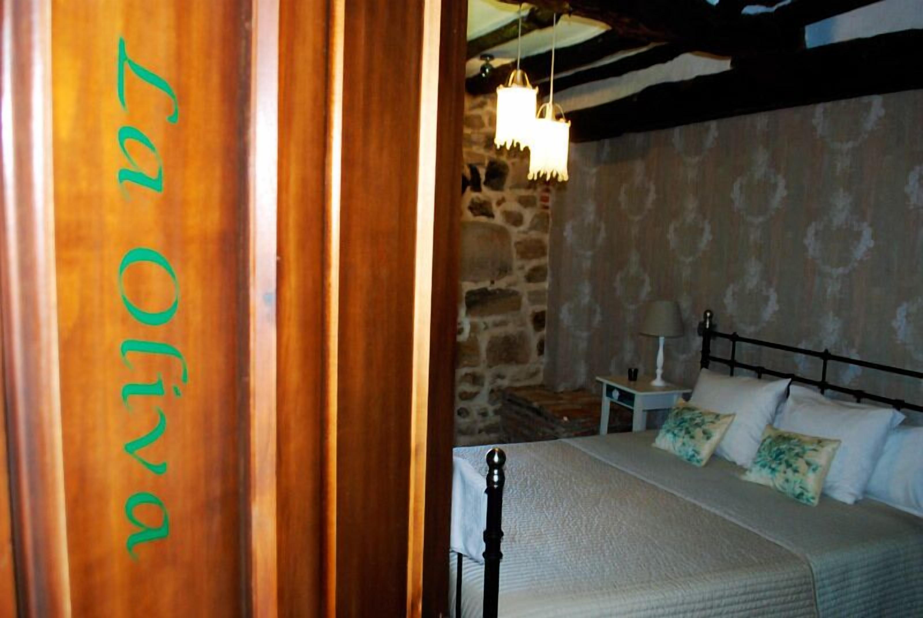 A bedroom with a bed, a nightstand, a lamp, and a stone wall.