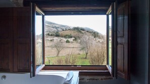 A room with a large window revealing a view of a hilly landscape with buildings and trees. - Posada La Corralada (Liérganes)