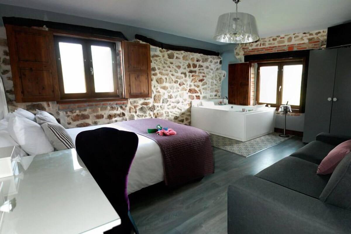 A bedroom with a bed, a desk, a sofa, and a bathroom with a bathtub.
