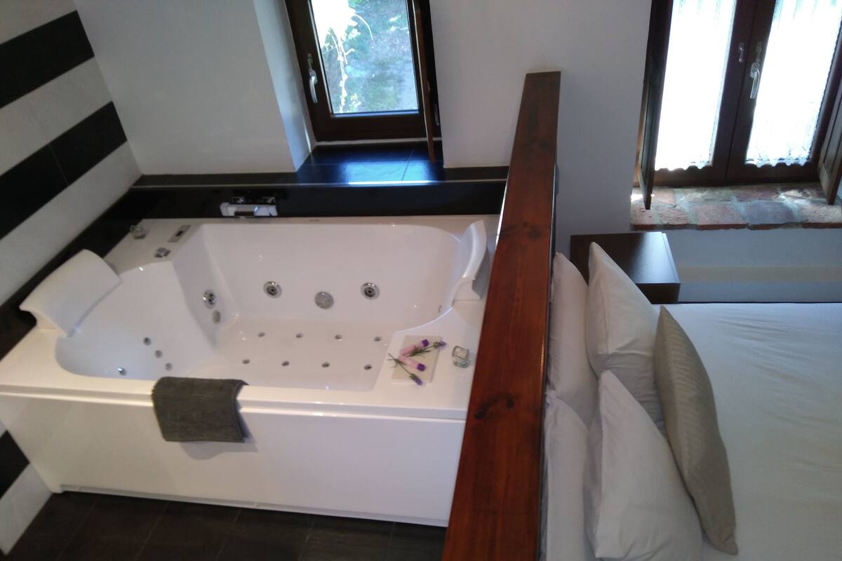 A modern bathroom with a large bathtub, a wooden bench, and a bed with white linens.