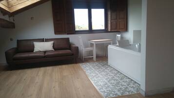 Een gezellige kamer met een bruine leren bank, een klein wit tafeltje en een raam met houten luiken.