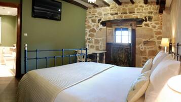 Een slaapkamer met een bed, een stenen muur, een houten deur en een aan de muur bevestigde televisie.