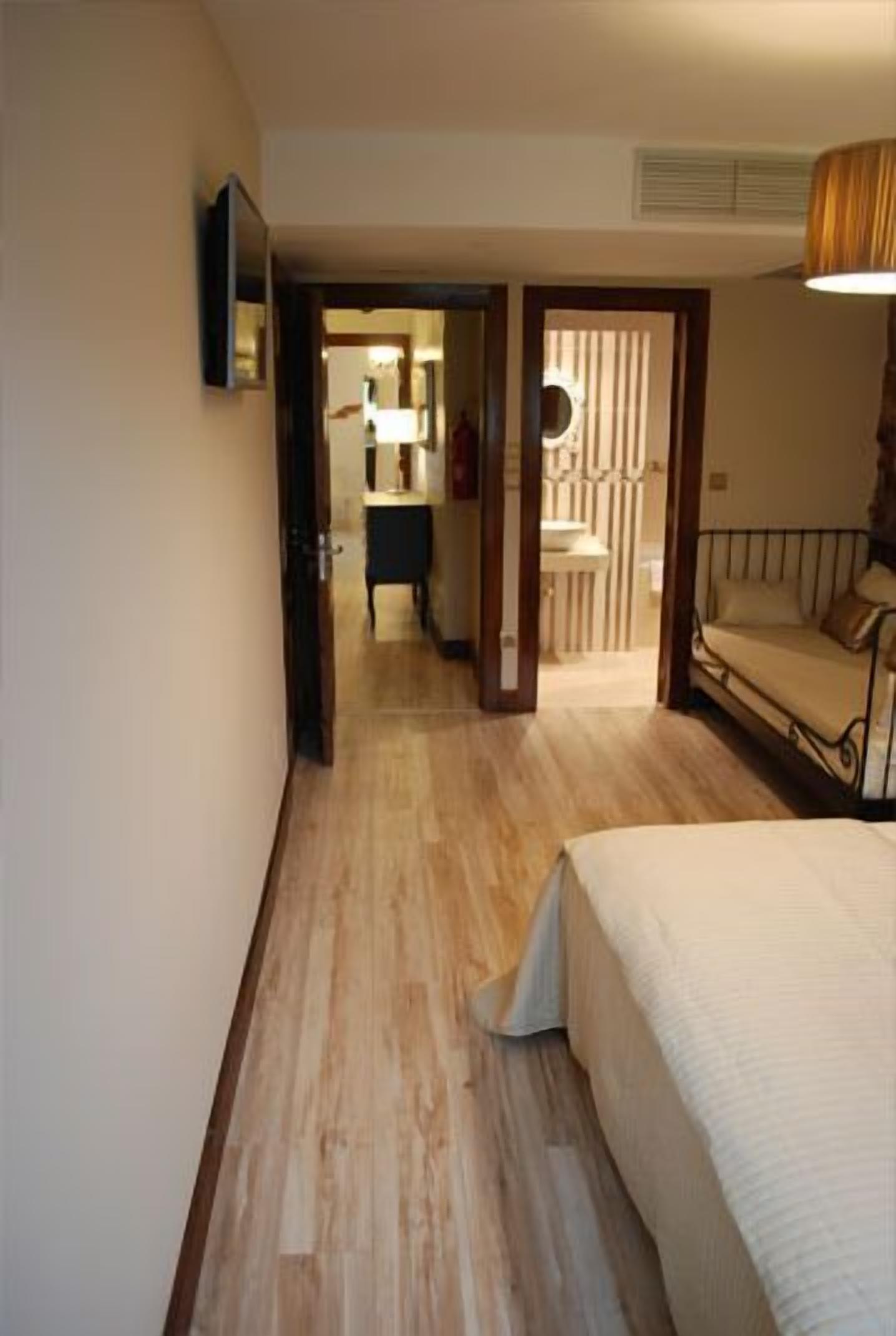 Una camera da letto con pavimento in legno, un letto, un comodino, uno specchio e una porta che dà su un bagno.