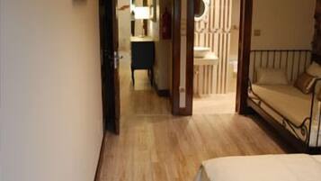 Una camera da letto con pavimento in legno, un letto, un comodino, uno specchio e una porta che dà su un bagno.