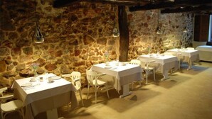 A dining area with stone walls and white tables, featuring hanging pendant lights and white chairs. - Posada La Corralada (Liérganes)