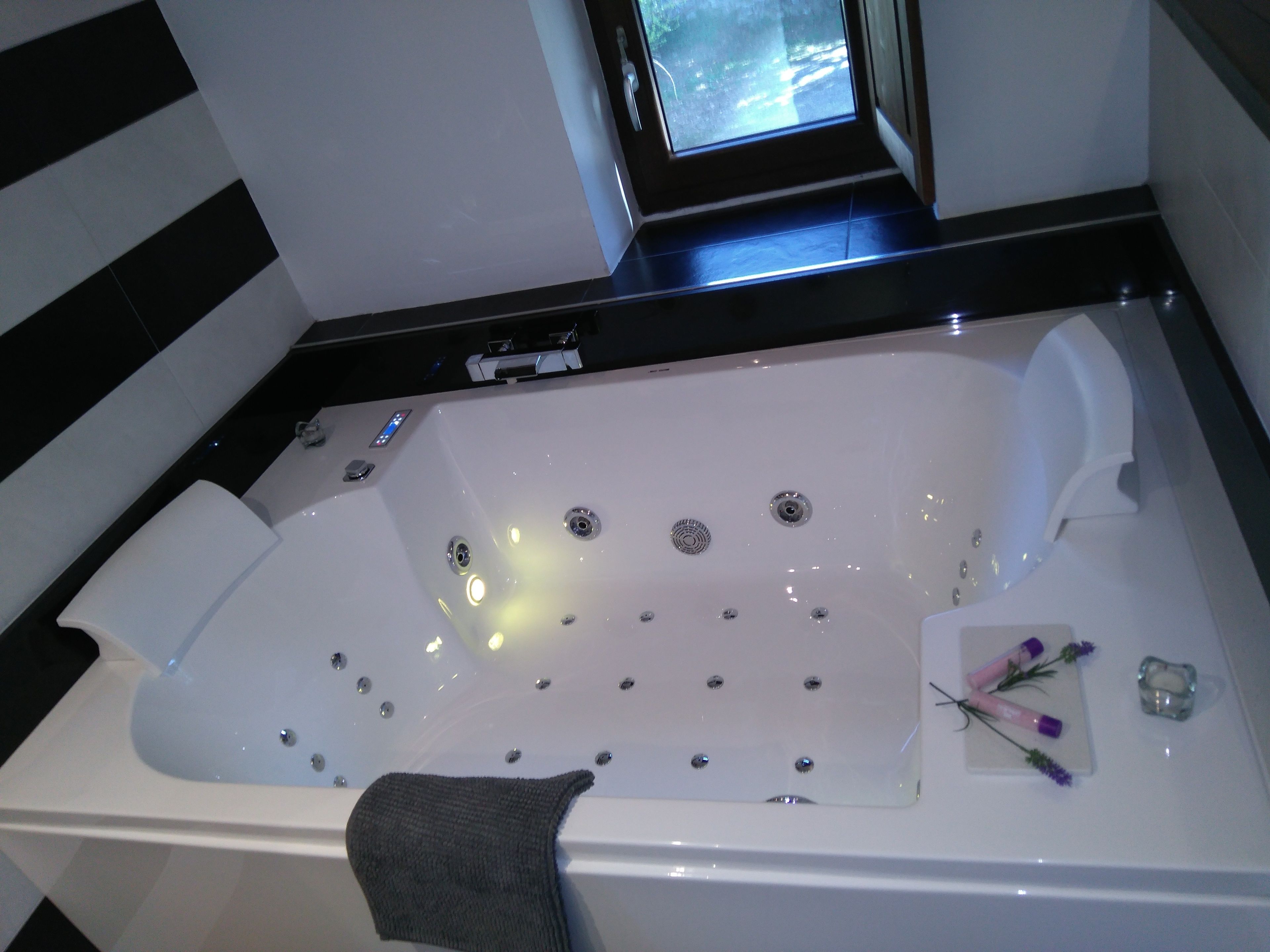Une baignoire blanche dotée de plusieurs jets, une fenêtre au-dessus et une serviette sur le bord.