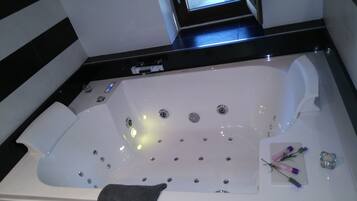 Une baignoire blanche dotée de plusieurs jets, une fenêtre au-dessus et une serviette sur le bord.