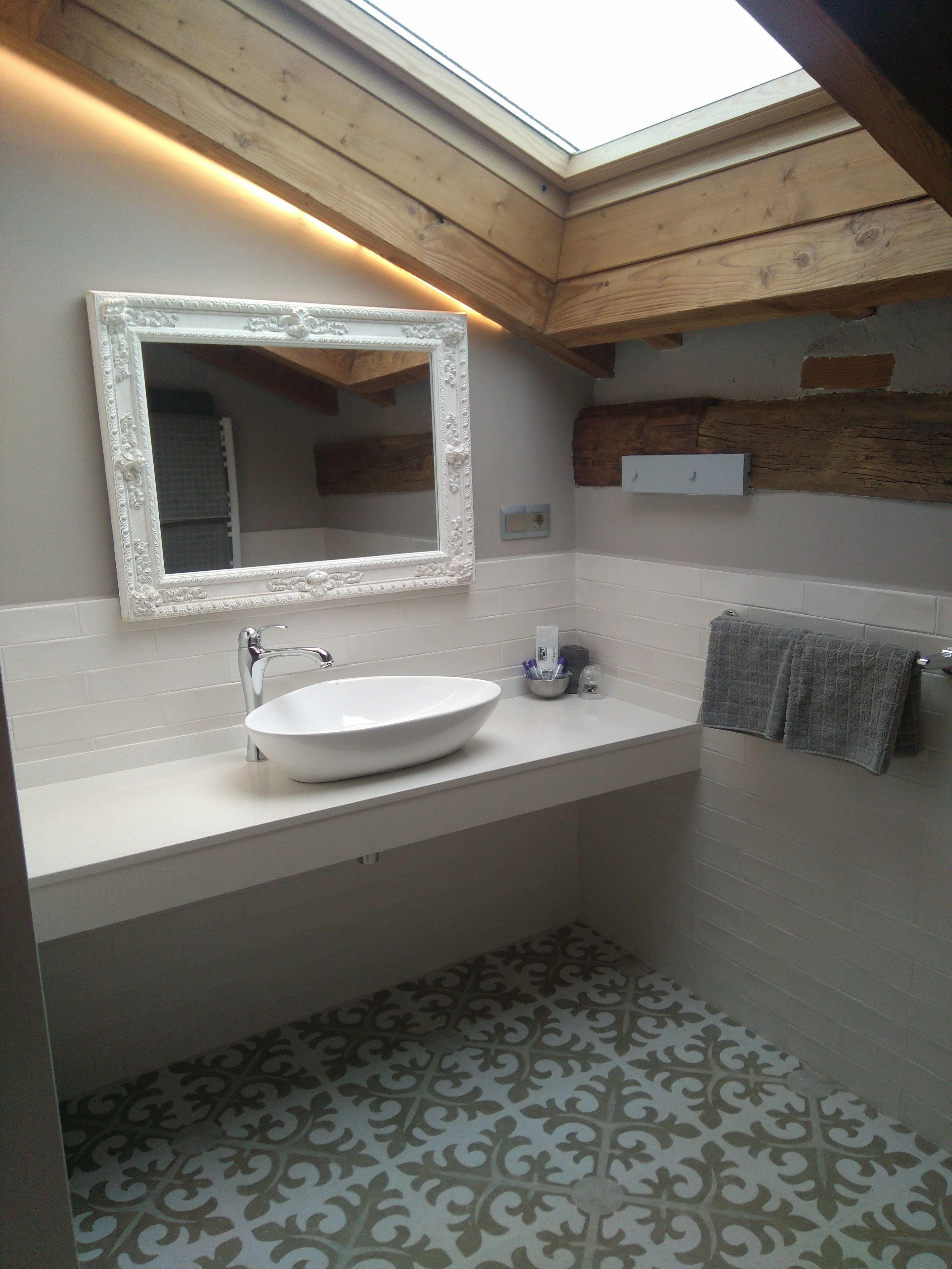 A modern bathroom with a skylight, a large mirror, a white sink, and patterned floor tiles.