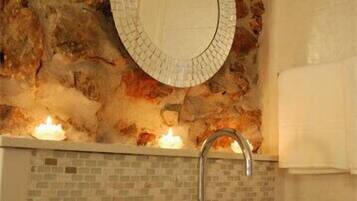 A bathroom with a stone wall, a round mirror, a sink, and candles.