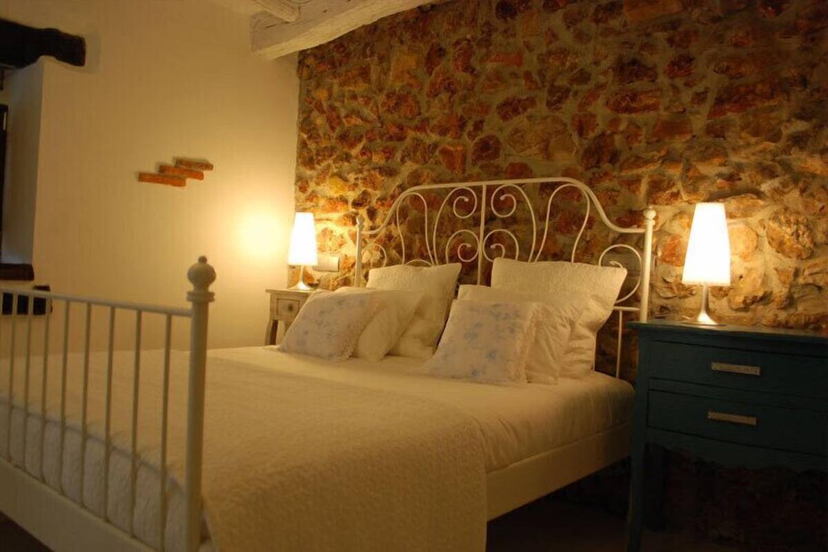 A bedroom with a stone wall, a white metal bed frame, and two bedside tables with lamps.