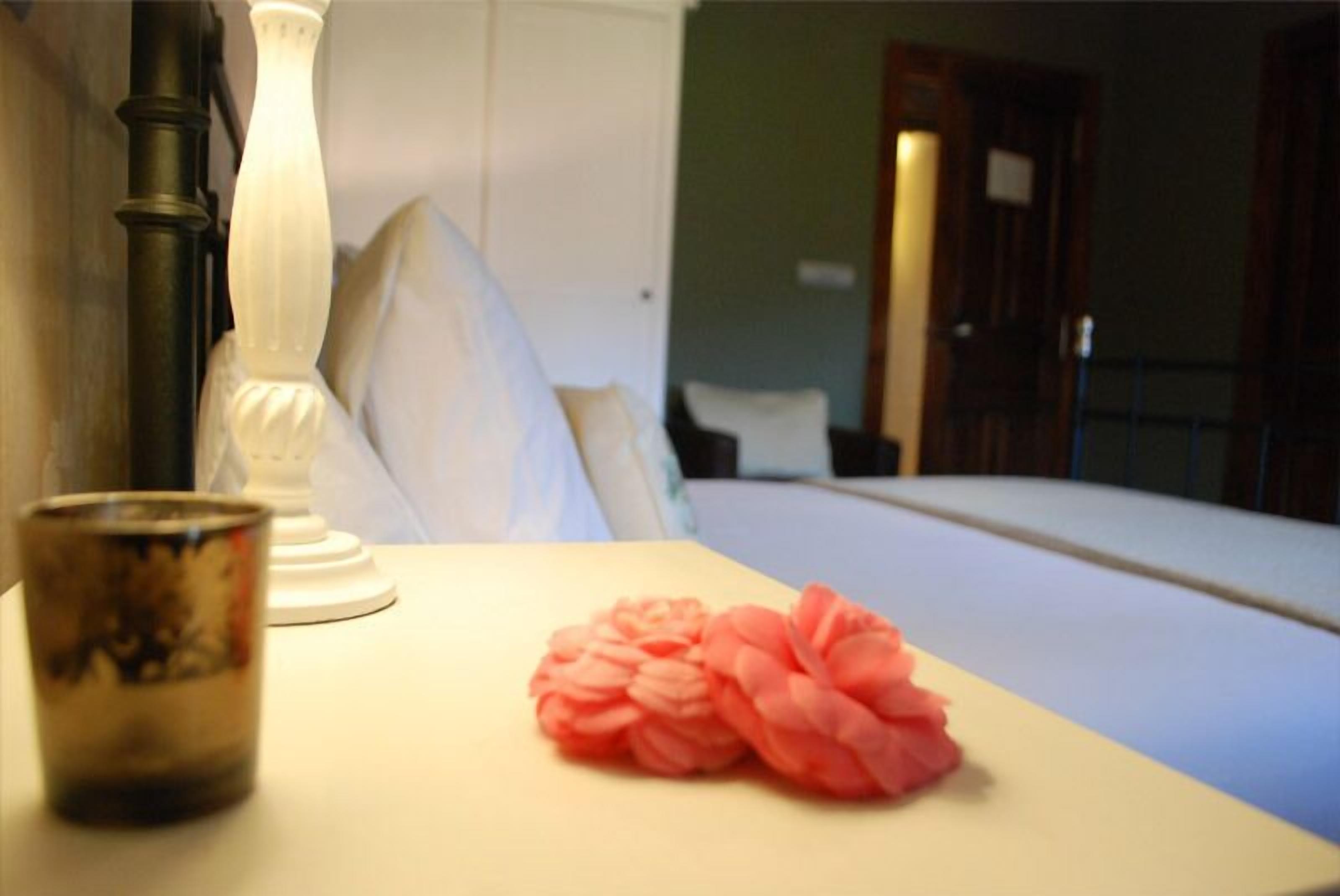 Una habitación de hotel con una cama, una mesita de noche, una lámpara y un objeto decorativo rosa.