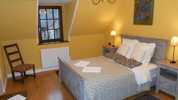 A bedroom with a bed, two bedside tables, a chair, a radiator, a window, and a chandelier.