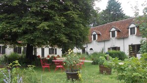 A courtyard with a white building, red chairs, and potted plants. - B&B La Ferme Des Bordes (Pontlevoy)