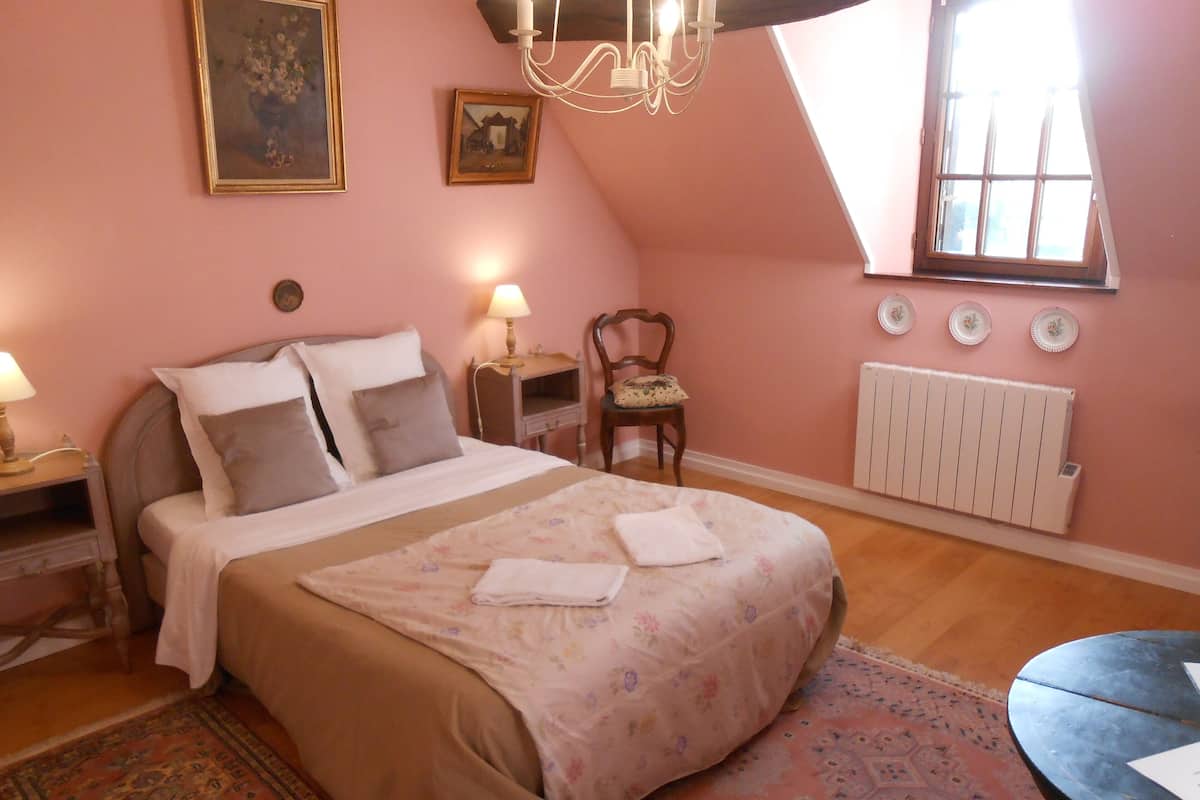 Un dormitorio con cama, mesitas de noche, una silla, un radiador y una ventana.