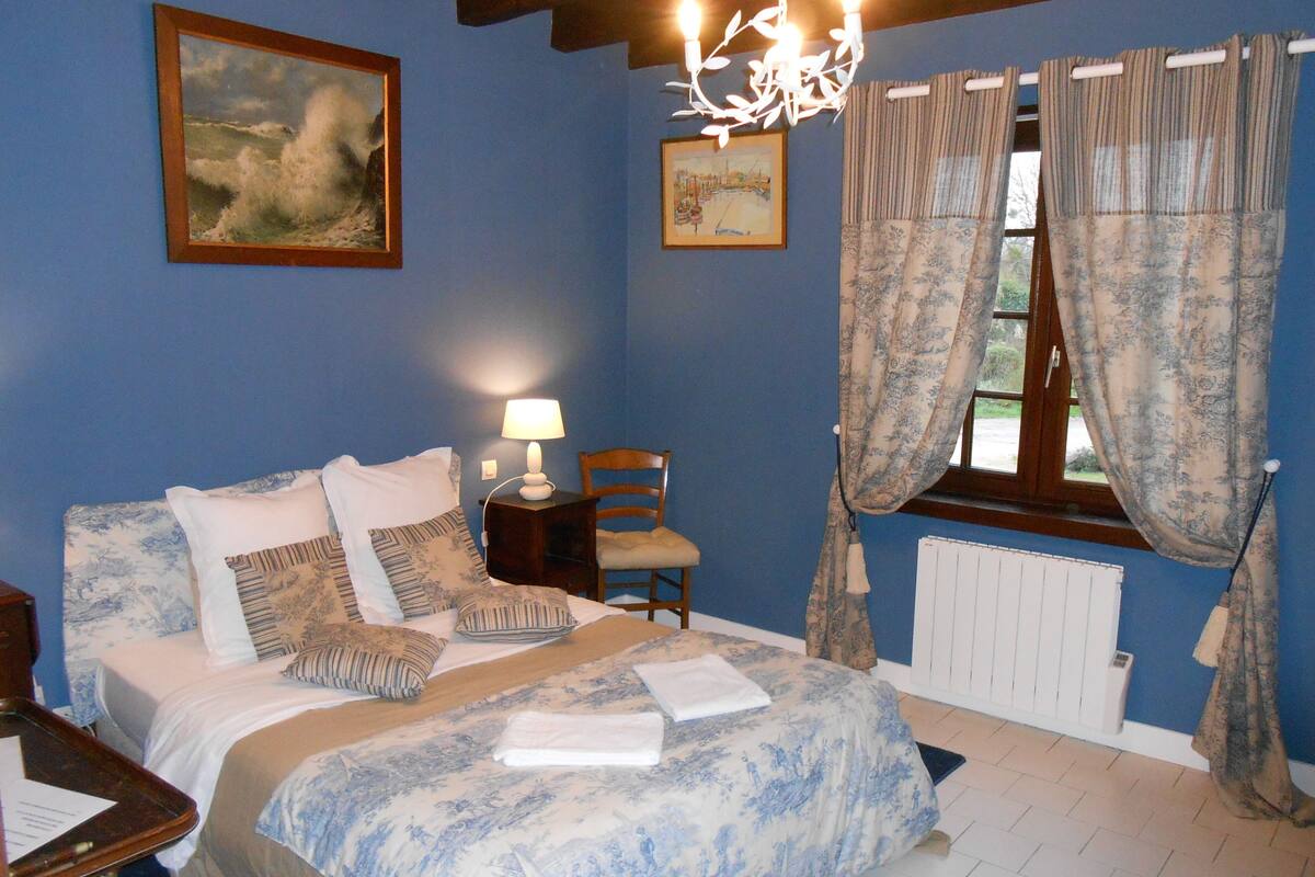 Un dormitorio con cama, una silla, una mesita de noche, una lámpara, una ventana con cortinas y un radiador.