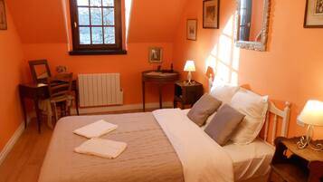Une chambre à coucher avec un lit, une chaise, une petite table, une table de chevet, un miroir et une fenêtre.