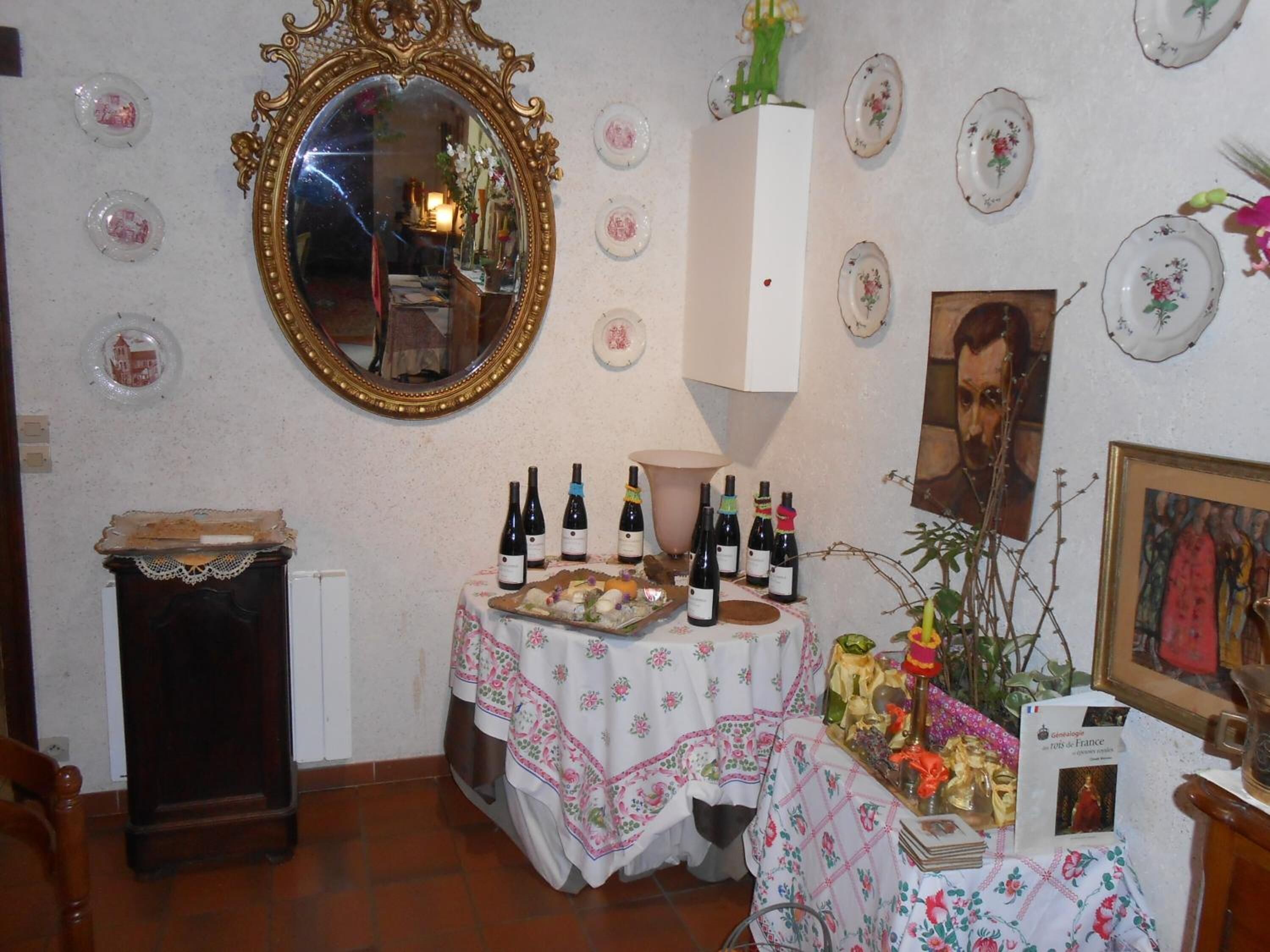 A room with a large ornate mirror, a table with wine bottles, decorative plates, and a framed portrait.
