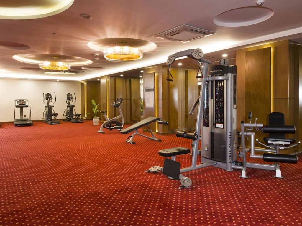 Uma academia com diversos equipamentos de exercício, piso revestido de carpete vermelho e design moderno no teto.