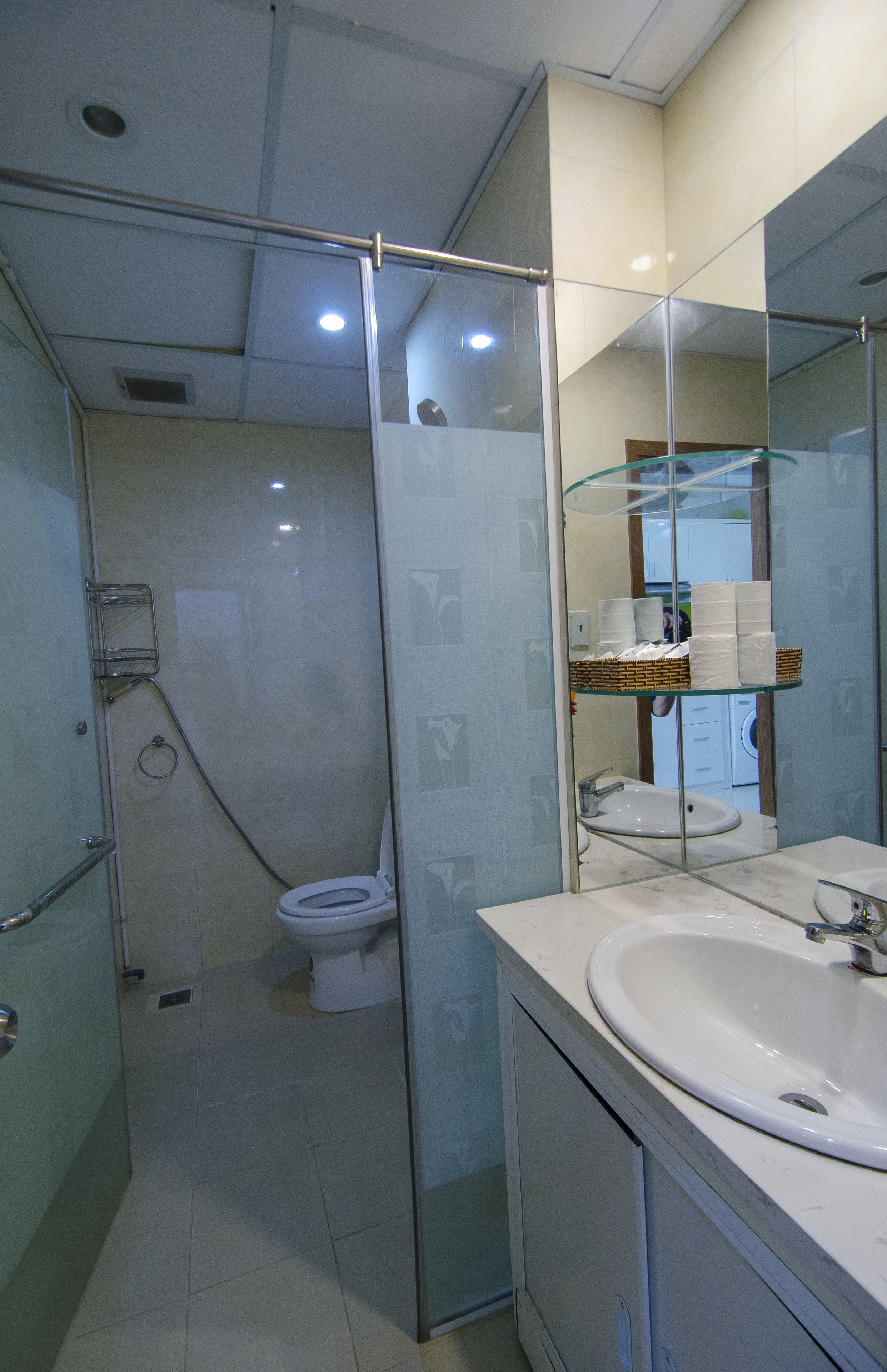 Un baño moderno con ducha de vidrio, inodoro blanco y un espejo grande sobre un lavamanos con encimera de mármol.