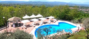 Une piscine entourée d’arbres, avec des chaises longues et des parasols, offrant une vue sur les montagnes lointaines.