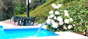 Une piscine agrémentée d’un élément décoratif aquatique, entourée de verdure et dotée d’un espace salon extérieur.