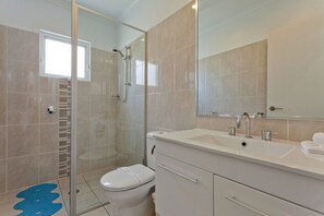 A modern bathroom with a glass-enclosed shower, a white toilet, and a vanity with a mirror.