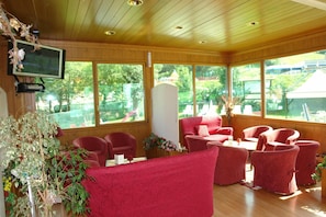Quarto com painéis de madeira, cadeiras estofadas em vermelho e uma televisão montada na parede.