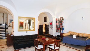 A spacious living room with a wooden dining table, a black leather sofa, and a blue sofa with striped cushions. There is a bookshelf filled with books and a painting on the wall. - Caio Mario (Rome)