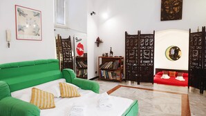 A hotel room with a green sofa bed, a red sofa bed, a bookshelf, and a decorative wall with a Buddha image. - Caio Mario (Rome)