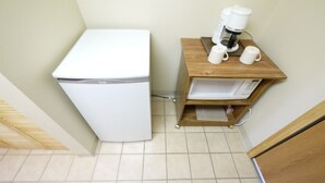 Une petite cuisine équipée avec un réfrigérateur blanc, une machine à café et un four à micro-ondes, le tout placé sur une étagère en bois.
