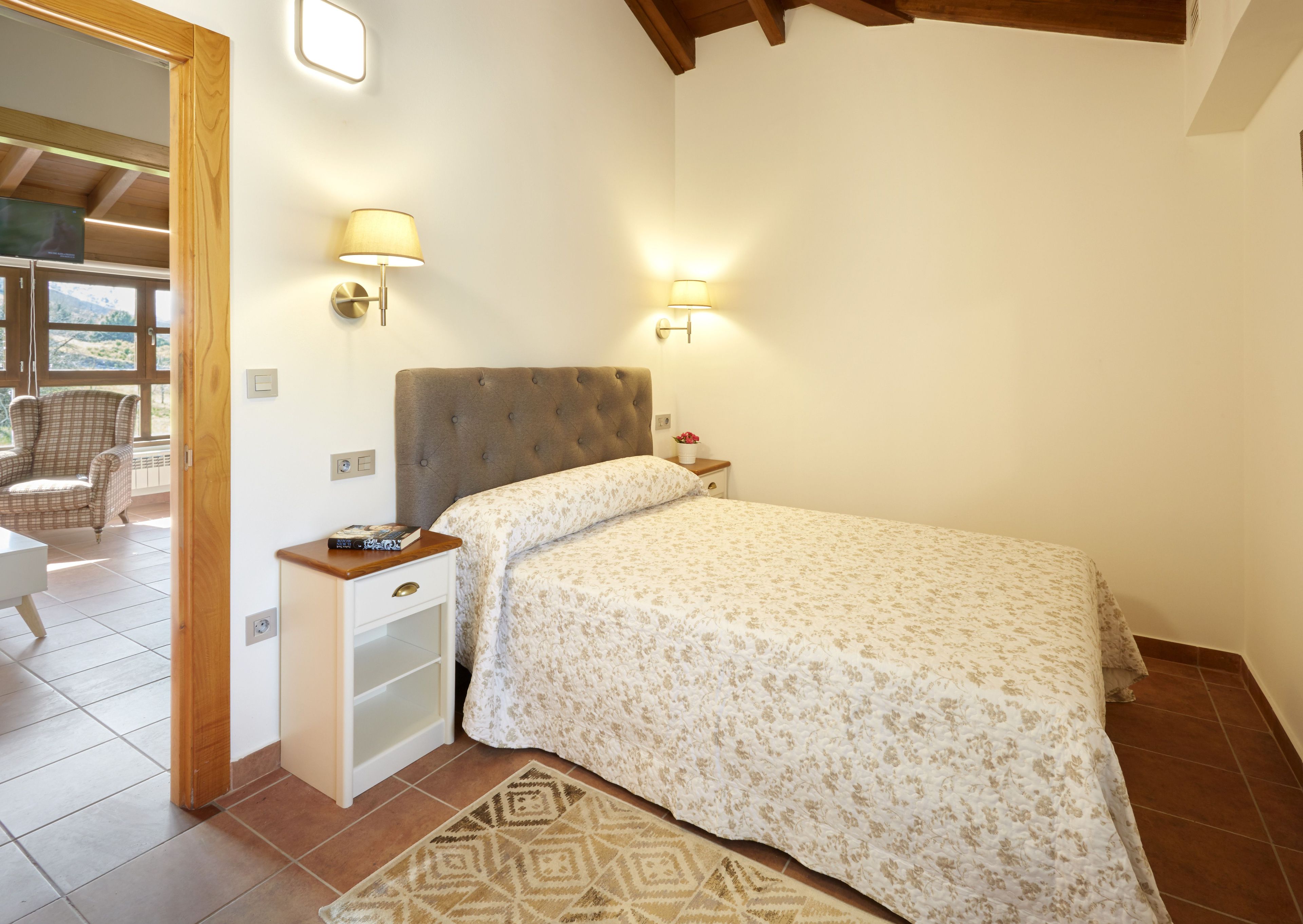 Un dormitorio con cama, lámparas de noche, una mesita de noche, una silla y vistas al exterior.