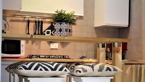 A kitchen with white cabinets, a microwave, a stove, and two bar stools with patterned cushions. - Riari Trastevere Apartment (Rome)