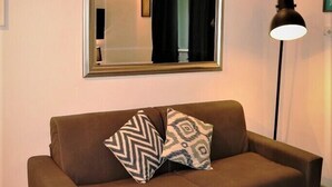 A brown sofa with patterned cushions, a large mirror on the wall, and a floor lamp. - Riari Trastevere Apartment (Rome)