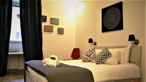 A neatly made bed with a grey blanket, a red chair, and a small table. - Riari Trastevere Apartment (Rome)