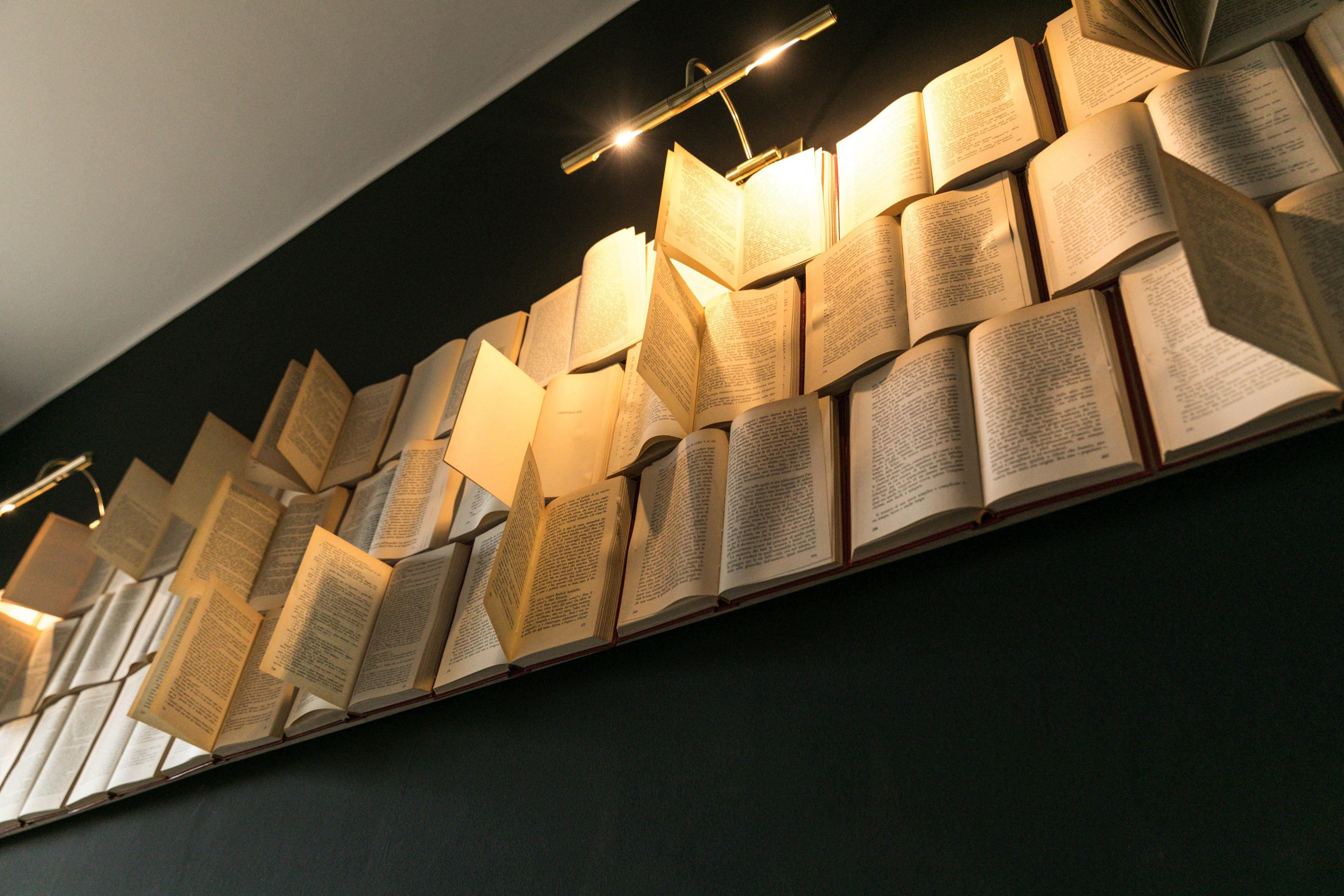 A wall of open books arranged in a staggered pattern, illuminated by overhead lighting.