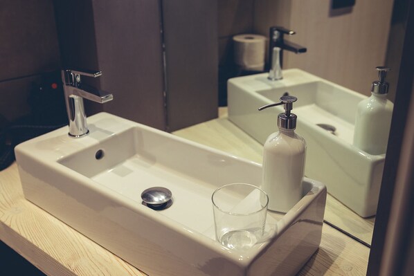 A bathroom with a white sink, a mirror, and a toilet paper roll in the background.