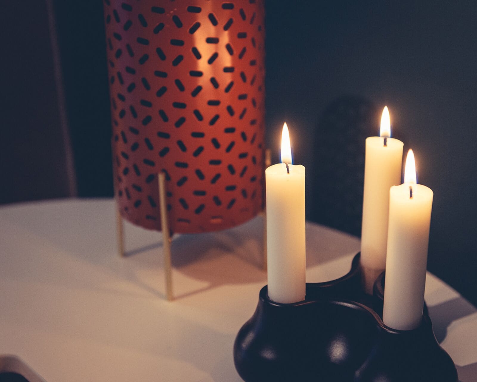 Three white candles in black holders on a table.