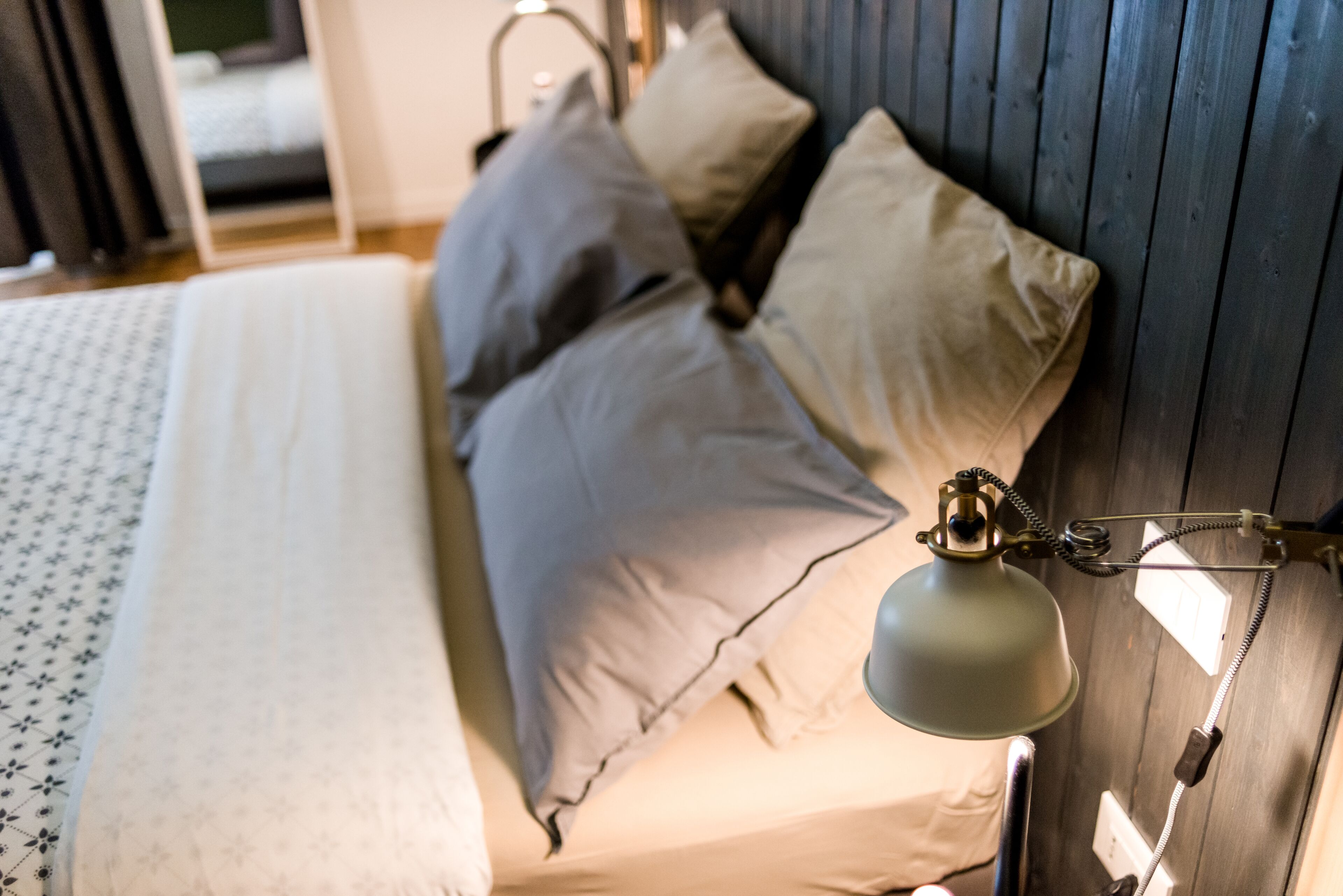 A bed with a patterned bedspread, multiple pillows, and a wall-mounted lamp.