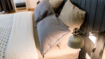 A bed with a patterned bedspread, multiple pillows, and a wall-mounted lamp.