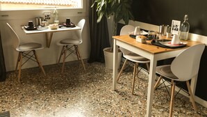 A dining area with a wooden table, white chairs, a potted plant, and a window with a view of buildings.