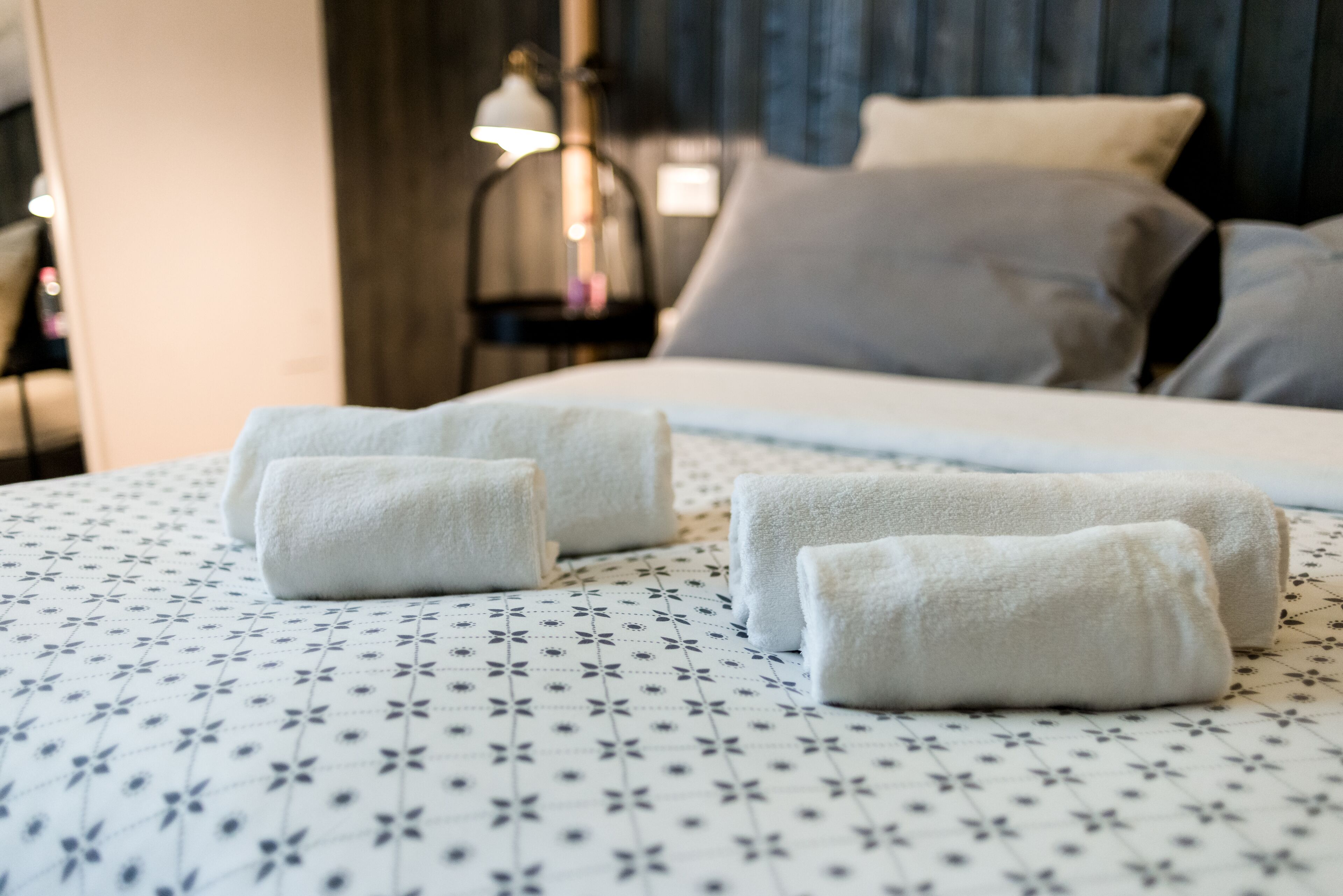 A neatly made bed with a floral-patterned bedspread and three folded towels.