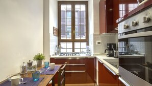 A modern kitchen with a window, stainless steel appliances, and a dining area with a table set for two. - Gianicolo's Hill Suite Apartment (Rome)