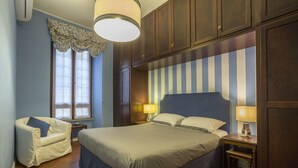 A bedroom with a large bed, a chair, a nightstand, and a window with curtains. - Gianicolo's Hill Suite Apartment (Rome)