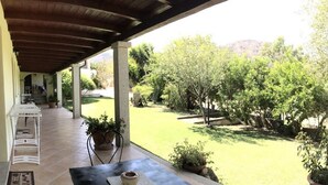Une terrasse couverte avec des sièges d’extérieur, une vue sur un jardin aménagé et une montagne en arrière-plan.