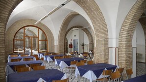 A spacious hall with high arched ceilings and brick walls, featuring tables set for dining and chairs arranged around them. - Pensione Piemonte (Loreto)
